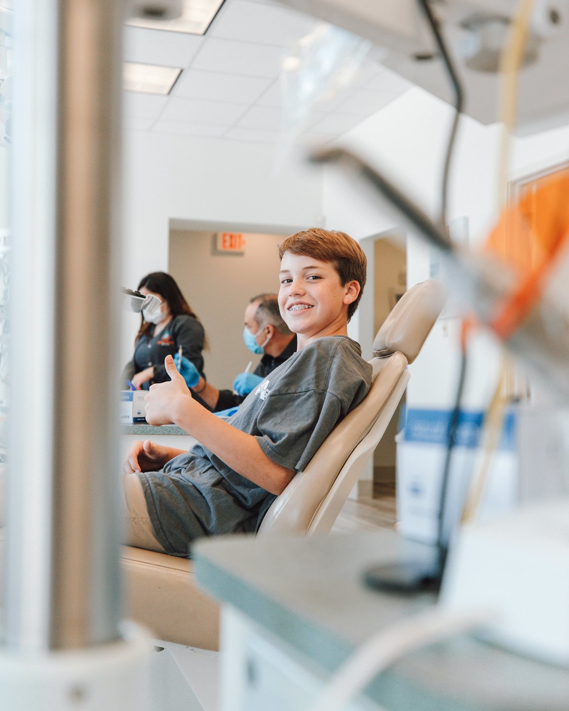 Un niño sonriente da el visto bueno en una silla de dentista.